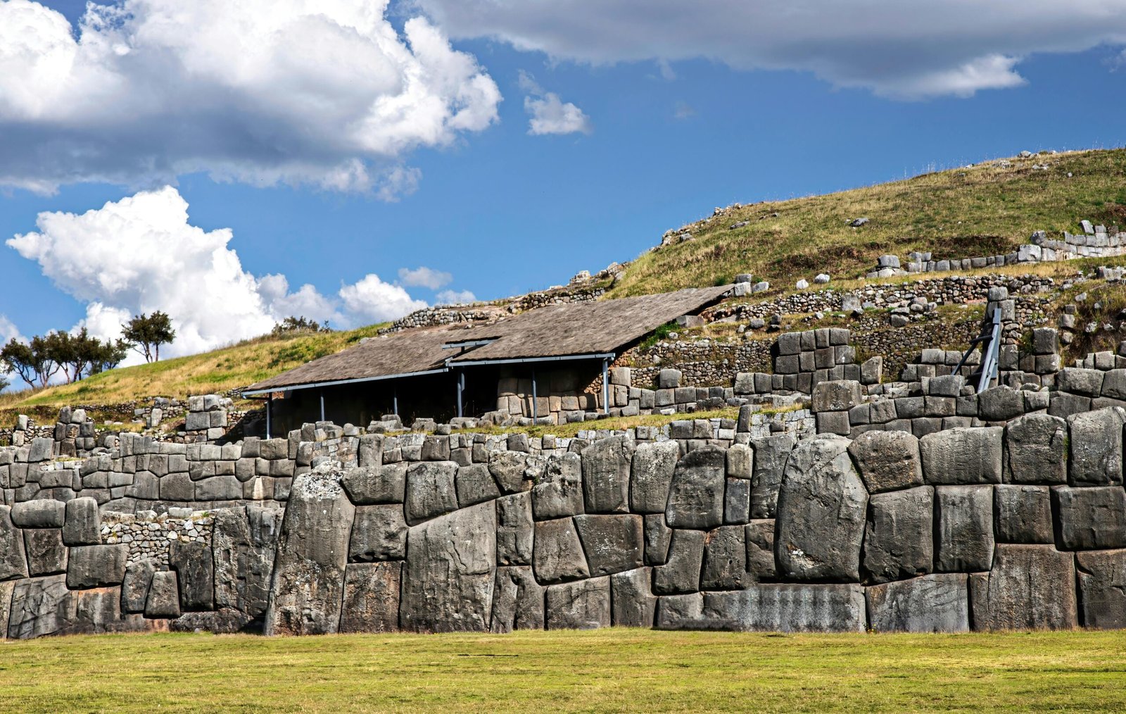 Explore the historic stone walls of Sacsayhuamán against a vibrant blue sky and lush grass.