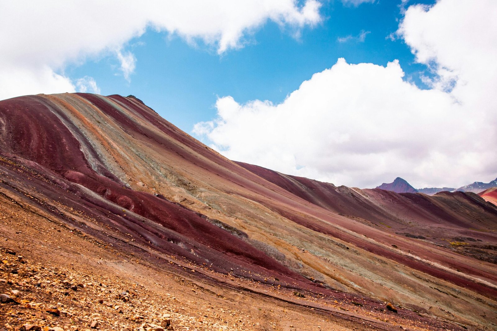 Colorful geological formations of Rainbow Mountain in Peru under a bright blue sky.