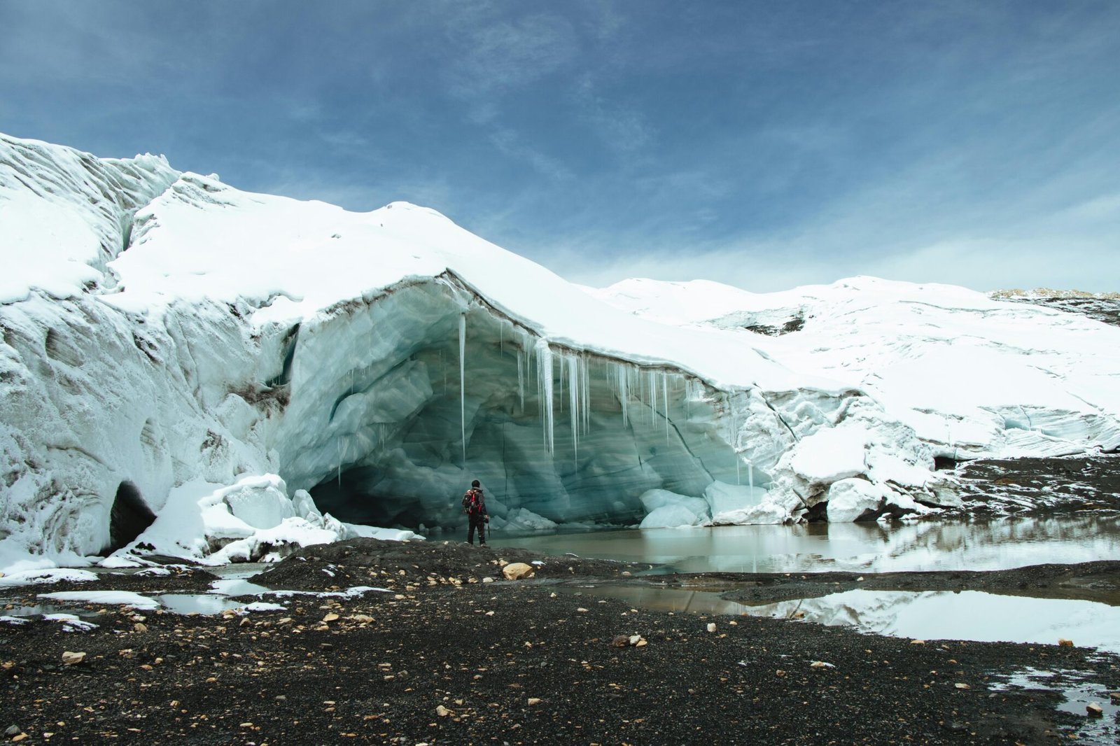 A lone hiker stands before the expansive Quelccaya Glacier in Cuzco, Perú, under a clear sky.
